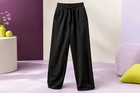 Pantalon de jogging noir à coupe droite et ample, taille haute ajustable, posé dans un studio aux tons prune et ivoire.