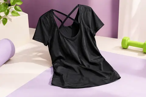 T-shirt de sport noir à manches courtes et dos ouvert croisé, posé sur un fond prune et lilas clair.