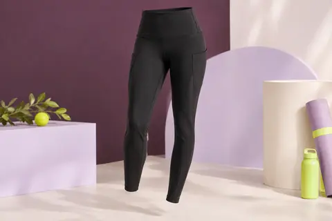 Legging de sport noir mat à taille haute et poches latérales, présenté sur un fond de studio prune et lilas.