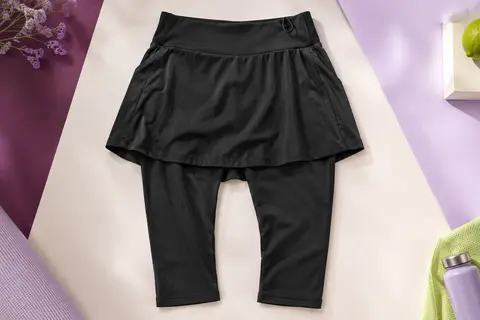 Jupe-short noire à taille haute avec legging 3/4 intégré et poches, posée sur un fond de studio lilas et prune.
