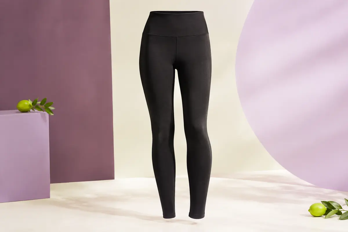 Legging de sport noir à taille haute présenté seul dans un studio lumineux aux tons prune et lilas.