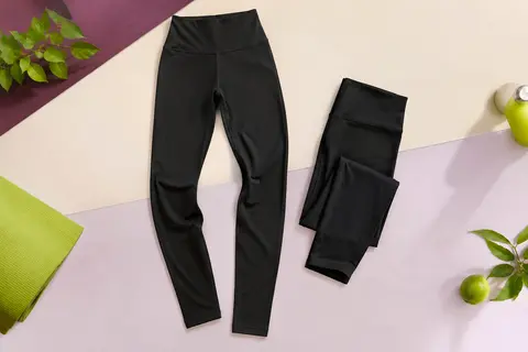 Deux leggings noirs taille haute en polyester, posés sur un fond de studio prune et ivoire.